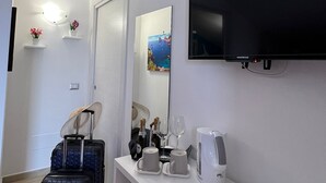Ein Hotelzimmer mit Flachbildfernseher, Minibar, Kaffeemaschine und Spiegel. Auf dem Boden liegen zwei Koffer und ein Hut.