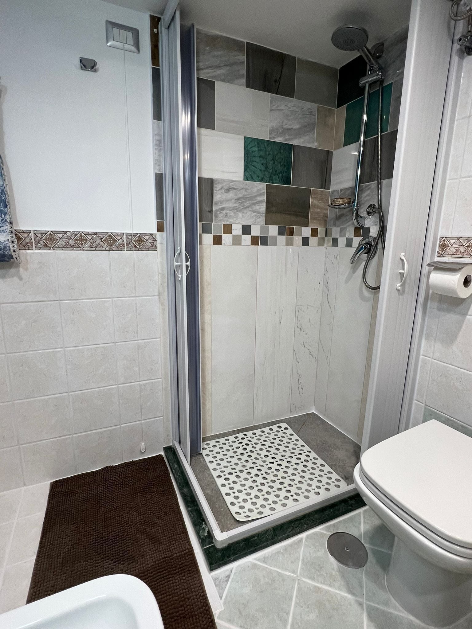 A shower with a glass door, a toilet, and a patterned tile backsplash.