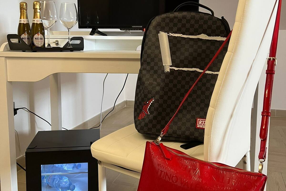Une chambre moderne avec un bureau blanc, une télévision, un sac à main rouge et un ordinateur portable.
