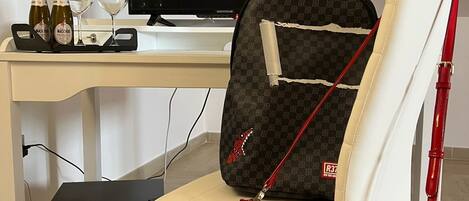 Una habitación moderna con un escritorio blanco, un televisor, un bolso rojo y una computadora portátil.