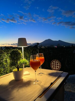 Ein Tisch mit zwei Gläsern Orangensaft und einer Lampe, vor einer Berglandschaft und blauem Himmel.