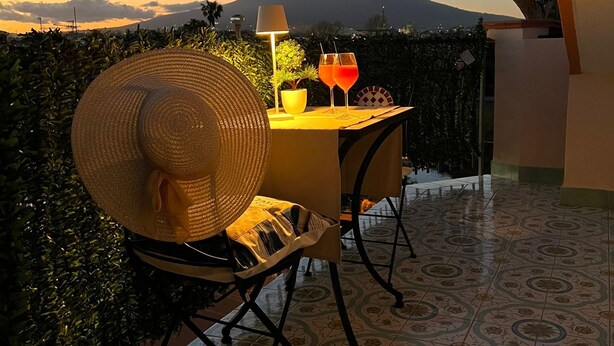 Ein Balkon mit Tisch für zwei Personen, ein großer gewebter Hut und zwei Getränke. Im Hintergrund ist ein Berg zu sehen.