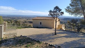 A small building with a tiled roof, surrounded by gravel and sparse vegetation, overlooking a rural landscape with distant hills and a clear sky. - Maison Ensoleillée, Grande Terrasse Avec vue Panoramique et Accès Piscine (Saint-Hippolyte-le-Graveyron)