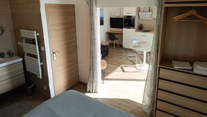 A modern bedroom with a wooden wardrobe, a bed, a desk, and a kitchenette. - Maison Ensoleillée, Grande Terrasse Avec vue Panoramique et Accès Piscine (Saint-Hippolyte-le-Graveyron)