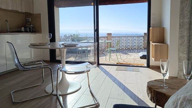A modern kitchen with a dining area, a balcony with a view of the sea, and a small seating area with a table and chairs. - Maison Ensoleillée, Grande Terrasse Avec vue Panoramique et Accès Piscine (Saint-Hippolyte-le-Graveyron)