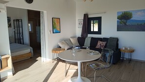 A modern living room with a round dining table, a sofa set, and a large window with a view of the outdoors. - Maison Ensoleillée, Grande Terrasse Avec vue Panoramique et Accès Piscine (Saint-Hippolyte-le-Graveyron)