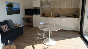 A modern kitchen with white cabinets, a built-in oven, and a dining area with a round table and chairs. - Maison Ensoleillée, Grande Terrasse Avec vue Panoramique et Accès Piscine (Saint-Hippolyte-le-Graveyron)