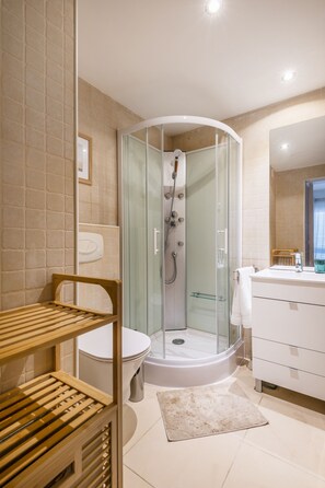 A modern bathroom with a glass-enclosed shower, a white toilet, and a wooden shelf. - Balaia 3BR Sunny Terrace (Albufeira)