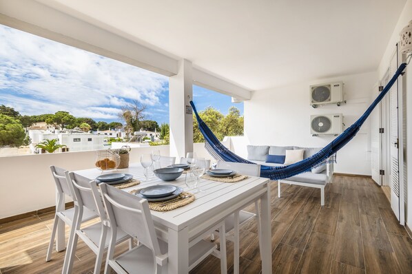 A terrace with a white table set for dining, a hammock, and a view of the surrounding area. - Balaia 3BR Sunny Terrace (Albufeira)