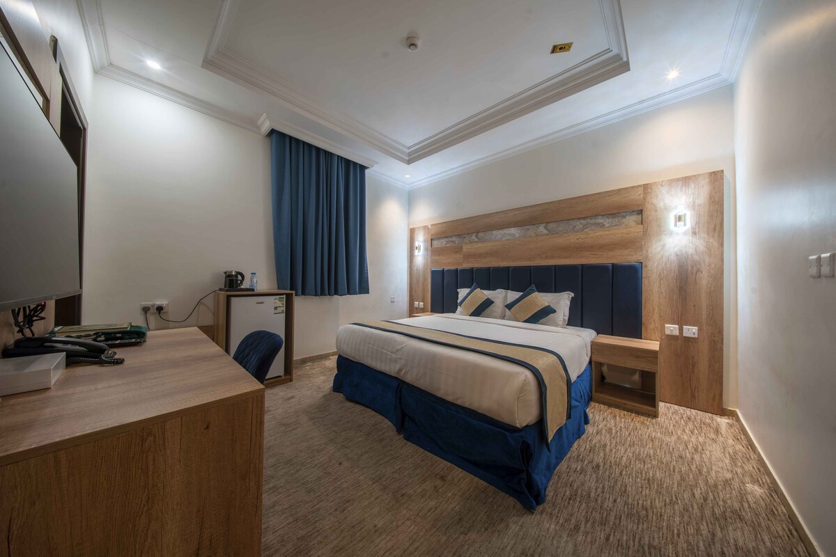 Een hotelkamer met een bed, een bureau, een stoel, een klein kastje en een raam met gordijnen.