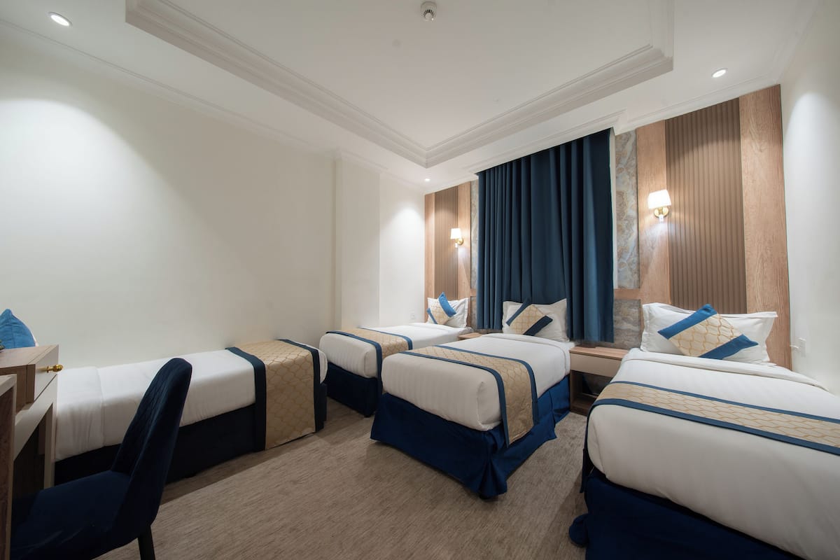 A hotel room with four single beds, a desk, and a chair.