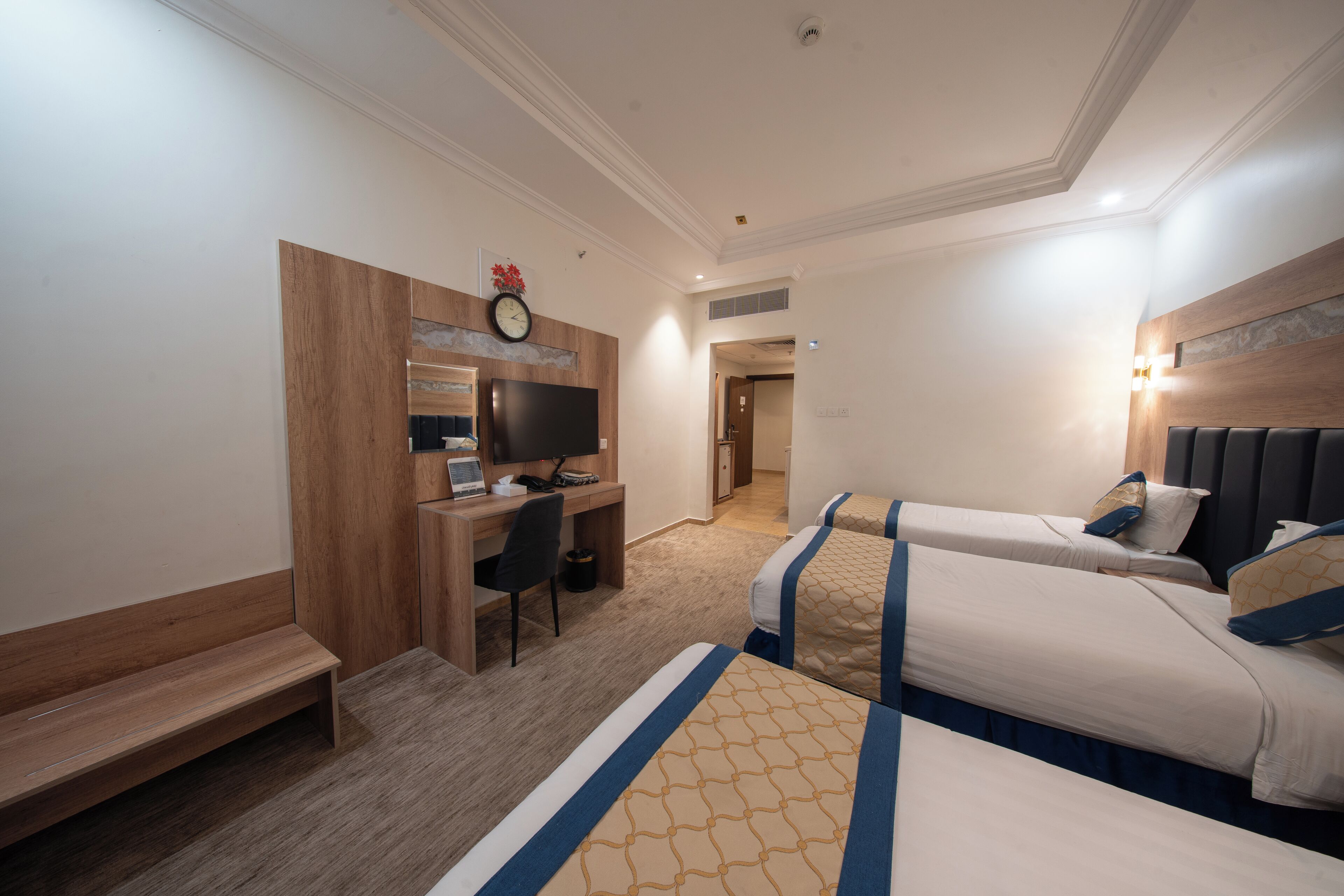 Ett hotellrum med ett skrivbord, två sängar, en väckarklocka och en tv.