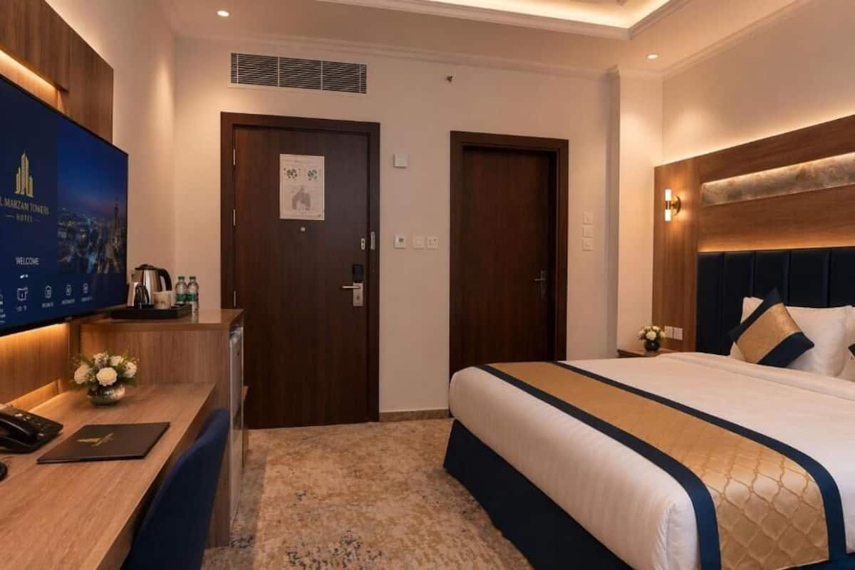 A hotel room with a bed, desk, television, and a door with a poster.