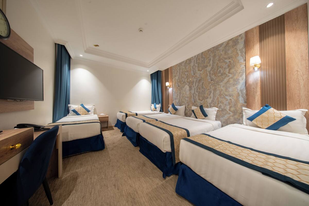 A hotel room with four beds, a desk, a chair, a TV, and a clock.