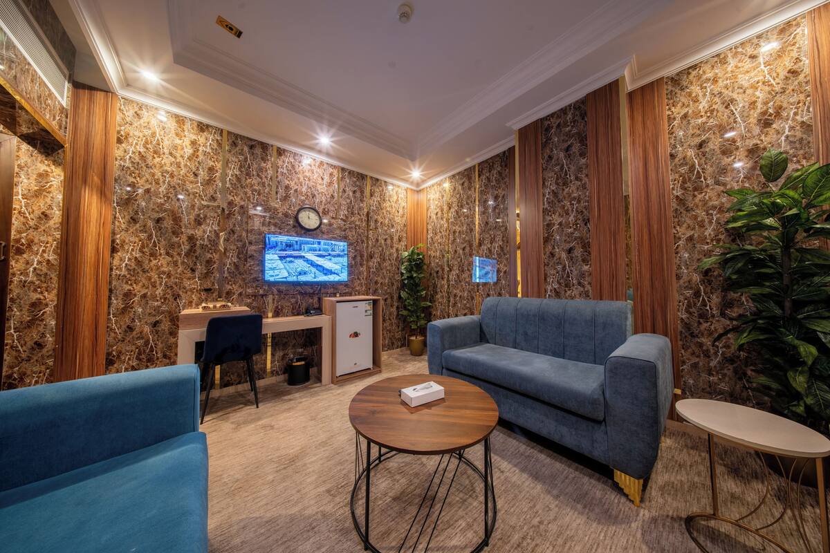 A modern hotel lobby with a marble wall, a blue sofa, a wooden desk, a computer, and a plant.