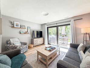 A modern living room with a flat-screen TV, two sofas, a coffee table, and a sliding glass door leading to an outdoor area.