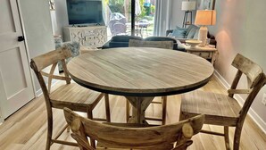 Una mesa de madera redonda con sillas, un televisor y vistas al exterior a través de una puerta corrediza.