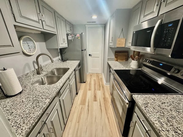 A kitchen with granite countertops, stainless steel appliances, and light wood flooring.