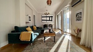 A modern living room with a dark green sofa, a coffee table, and a large window allowing natural light. - Spacious 2 Bedrooms Apartment With Acropolis View In Center of Athens (Athina)