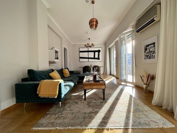 A modern living room with a dark green sofa, a coffee table, and a large window allowing natural light. - Spacious 2 Bedrooms Apartment With Acropolis View In Center of Athens (Athina)