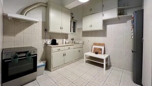 A compact kitchen with white cabinets, a built-in oven, a refrigerator, and a small bench. - Spacious 2 Bedrooms Apartment With Acropolis View In Center of Athens (Athina)