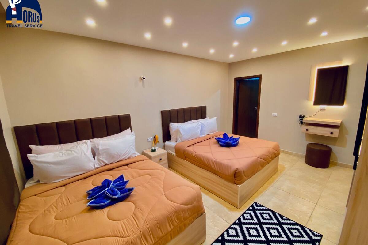 A hotel room with two beds, a bedside table, a mirror, and a small stool.