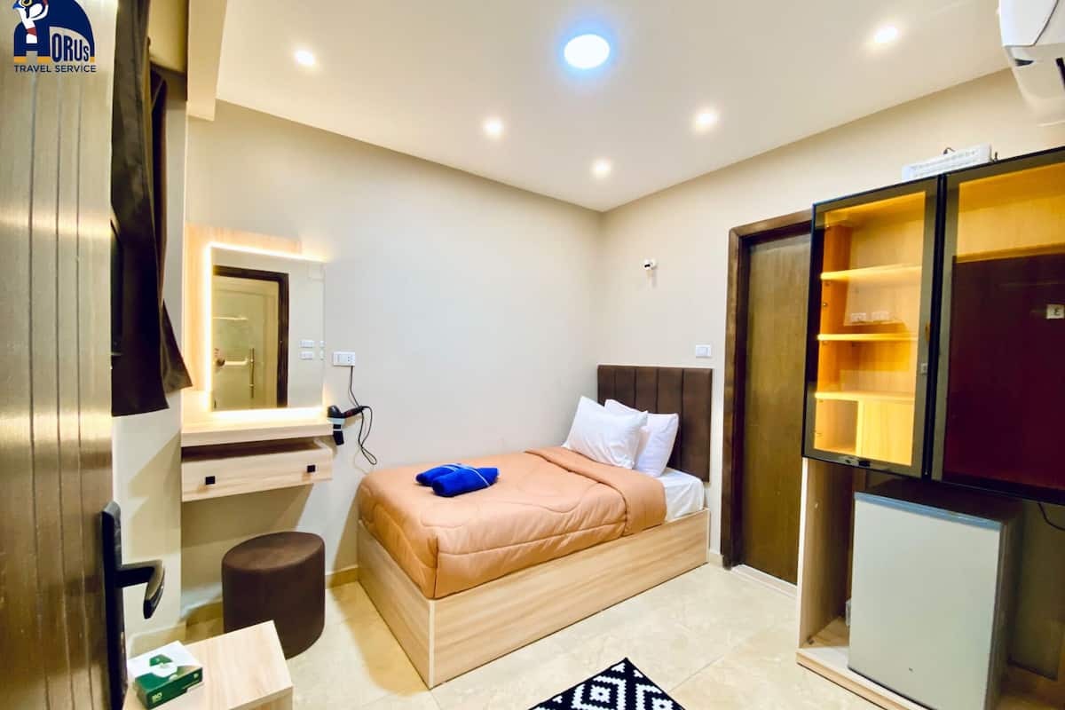 A modern hotel room with a bed, a small desk, a mirror, a wardrobe, and a mini-fridge.