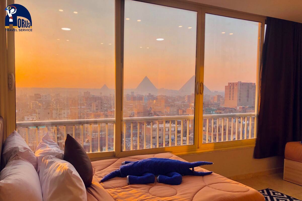 A hotel room with a large window offering a view of a cityscape and a mountain.