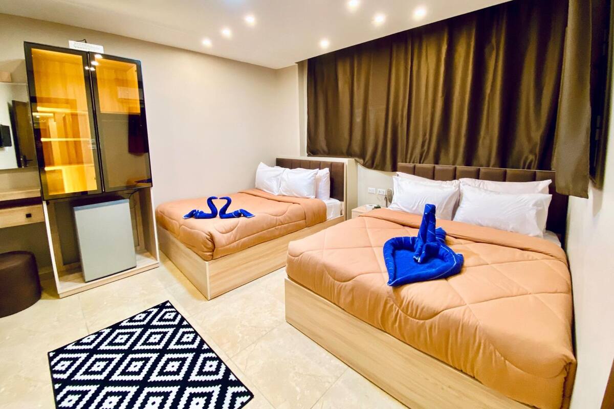 A hotel room with two beds, a desk, a refrigerator, and a patterned rug.
