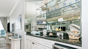 A modern kitchen with a glass-fronted island, white cabinetry, and a sign reading 'The beach is calling and I must go.' - Pearl of Navarre 402 | Gulf front condo | Resort Amenities and More (Navarre Beach)