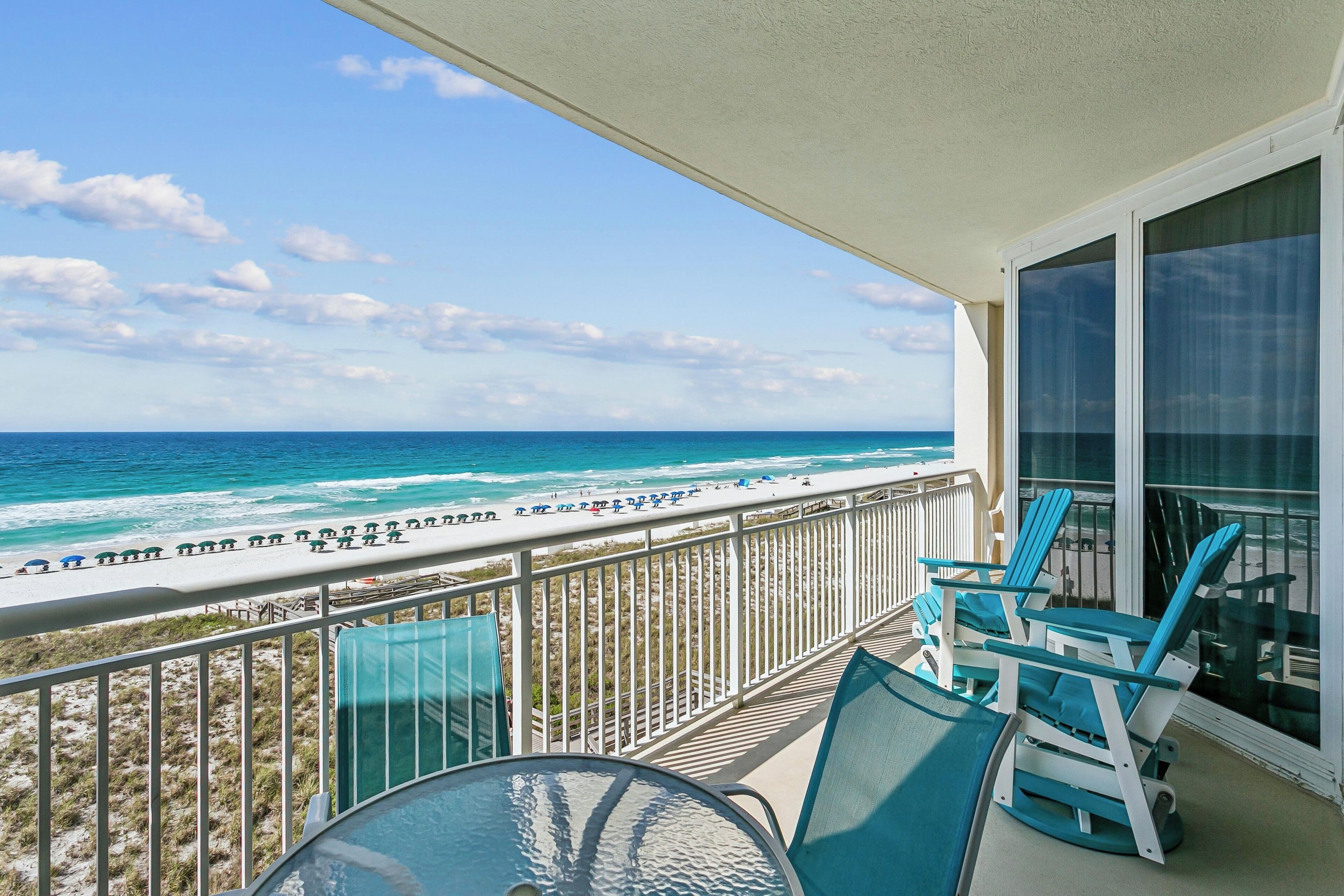 A balcony with a view of the ocean, a table, and blue chairs.