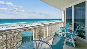 A balcony with a view of the ocean, a table, and blue chairs. - Pearl of Navarre 402 | Gulf front condo | Resort Amenities and More (Navarre Beach)