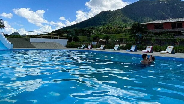 A swimming pool with lounge chairs and a mountain in the background. - Guarapari Park (Guarapari)