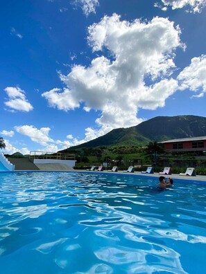Una piscina con sillas de descanso y una montaña al fondo.