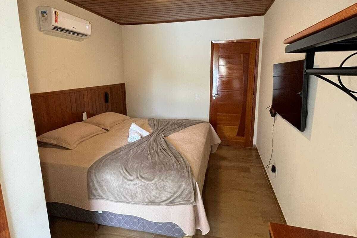 Une chambre de taille modeste, avec un lit, un téléviseur fixé au mur et un plafond en bois.