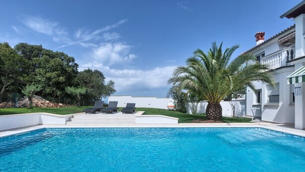 A swimming pool with lounge chairs, a palm tree, and a building in the background. - Comfortable Villa Ajda with sea view and heated pool (Pula)