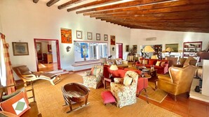A spacious living room with a high ceiling, wooden beams, and a variety of seating including a sofa, armchairs, and a rocking chair.
