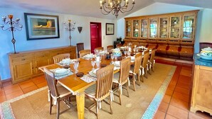A dining room with a long wooden table set for a meal, flanked by wooden cabinets and a chandelier.