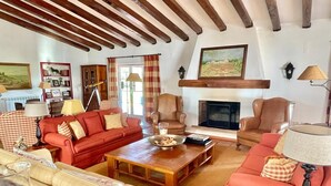 A cozy living room with a fireplace, red and beige sofas, wooden coffee table, and a bookshelf.