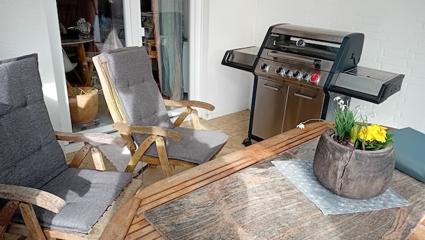 Un espacio de patio con una parrilla, dos sillas y una planta en maceta.