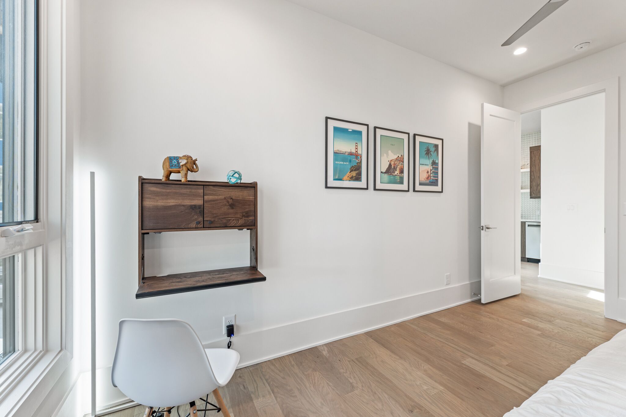 Une chambre moderne avec une commode en bois, une chaise blanche et trois tableaux encadrés accrochés au mur.