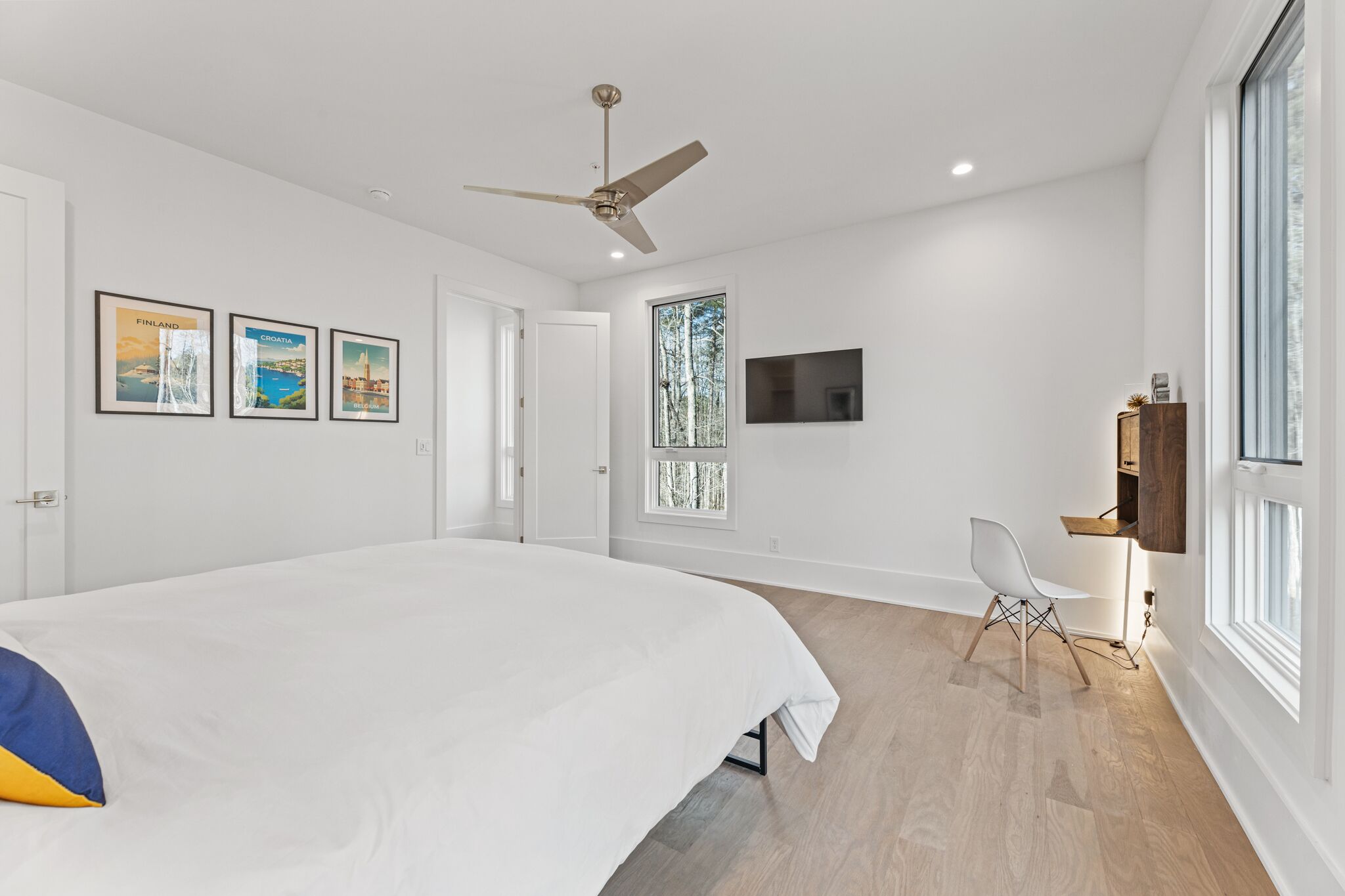 Une chambre moderne avec un grand lit, un ventilateur de plafond, des tableaux encadrés accrochés au mur, une télévision et un bureau avec une chaise.