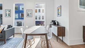 A modern living room with a dining table, white chairs, a grey sofa, and a coffee machine. - Plutus' Playhouse (Palmetto)