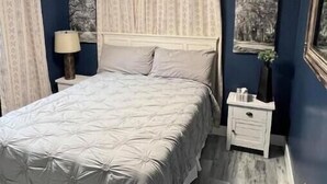 Ein Schlafzimmer mit einem Bett, einem Nachttisch, einer Lampe und zwei gerahmten Bildern an der Wand.
