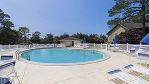Zona de piscina amb gandules i ombrelles, envoltada per una tanca blanca i arbres.
