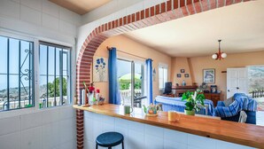 Una cocina con mostrador de madera, dos taburetes de bar, un arco de ladrillo y una zona de comedor con mesa y sillas.