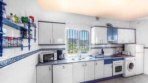 Una cocina con armarios blancos, microondas, lavadora y ventana con vistas a zonas verdes.