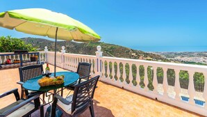Una terraza con mesa, sillas y un paraguas verde con vistas a un paisaje costero.