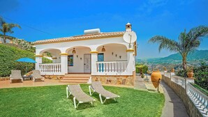 A two-story house with a balcony, a lawn with two sun loungers, and a view of the countryside. - Villa Los Sanchez - Two Bedroom Villa, Sleeps 4 (Frigiliana)