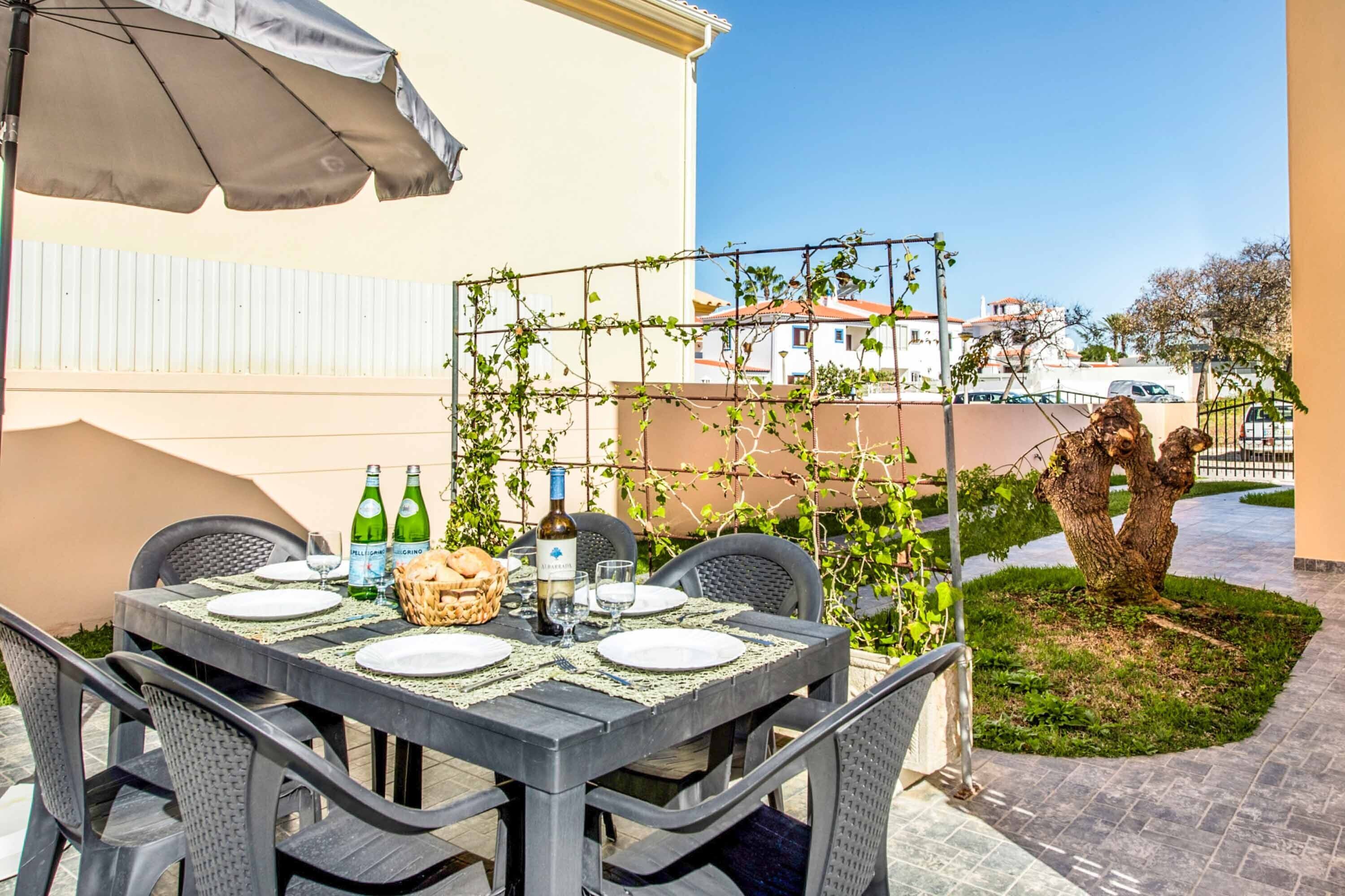 An outdoor dining area with a table set for four, surrounded by wicker chairs, under a large umbrella.